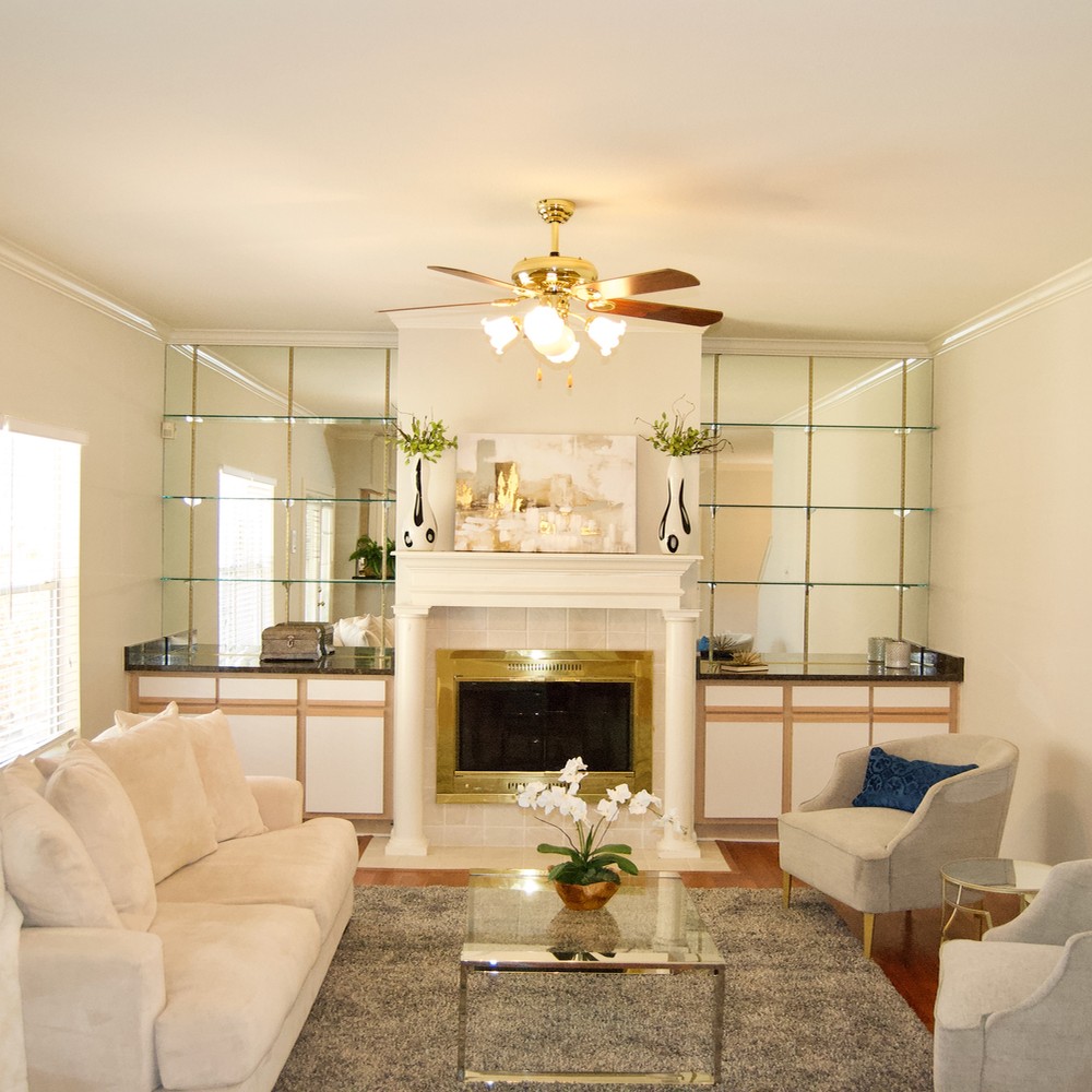 Living room with blue rug, white sofa with white pillows, glass coffee table, and two gray chairs with blue pillows.