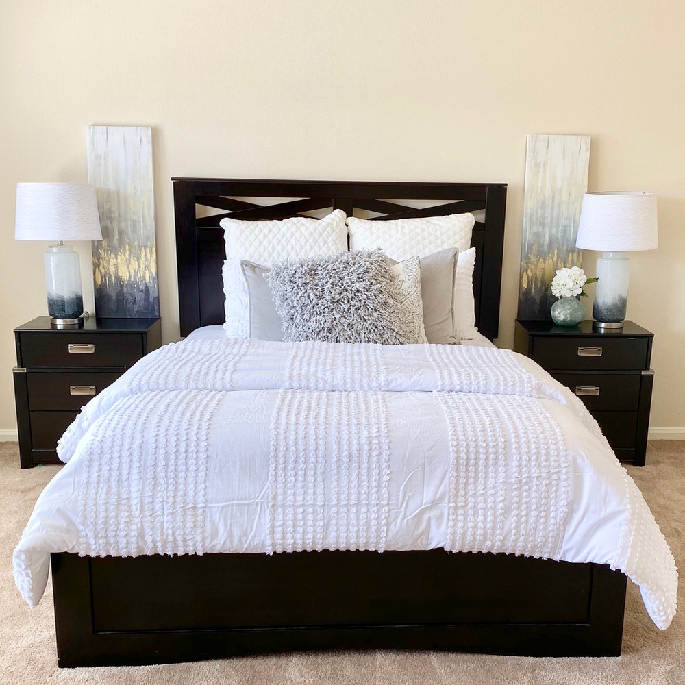 Primary bedroom with black wood bed frame. White comforter, black nightstands, white and blue lamps.