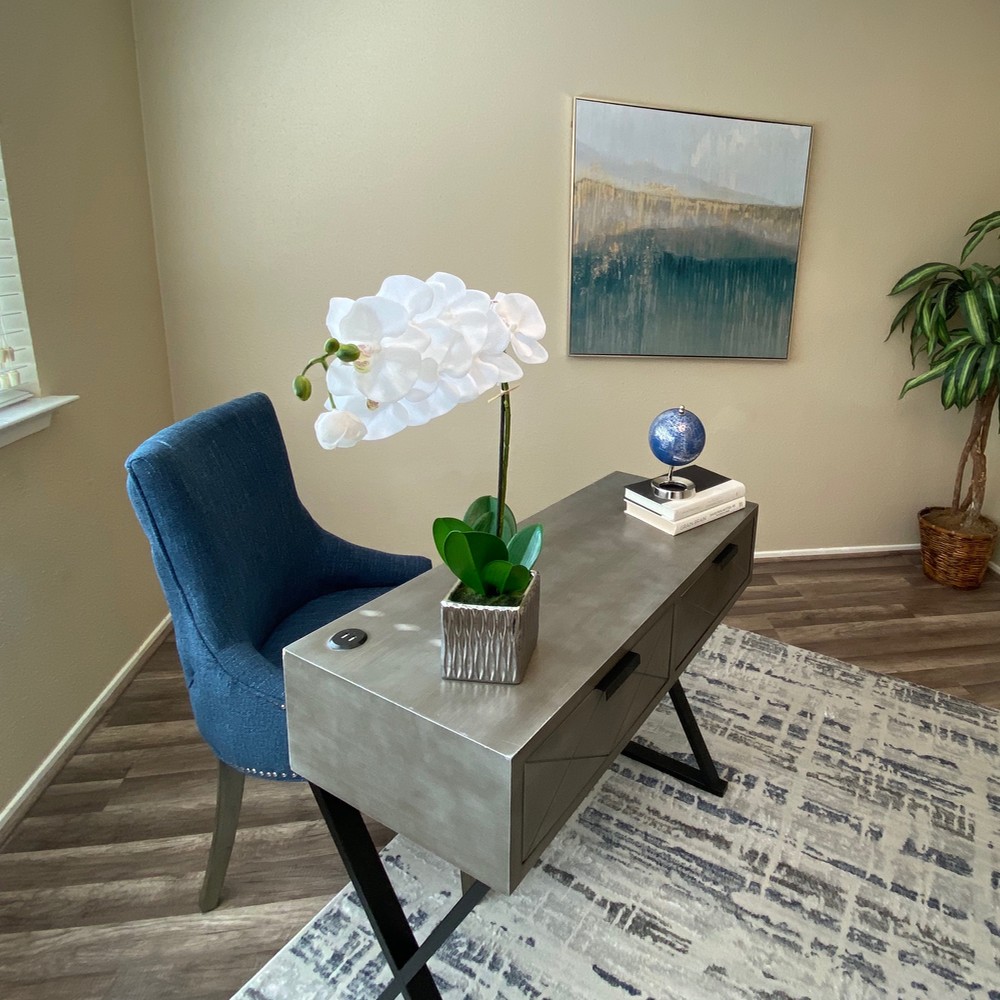 Office area with wooden desk. Blue and white rug. Blue chair behind the desk.