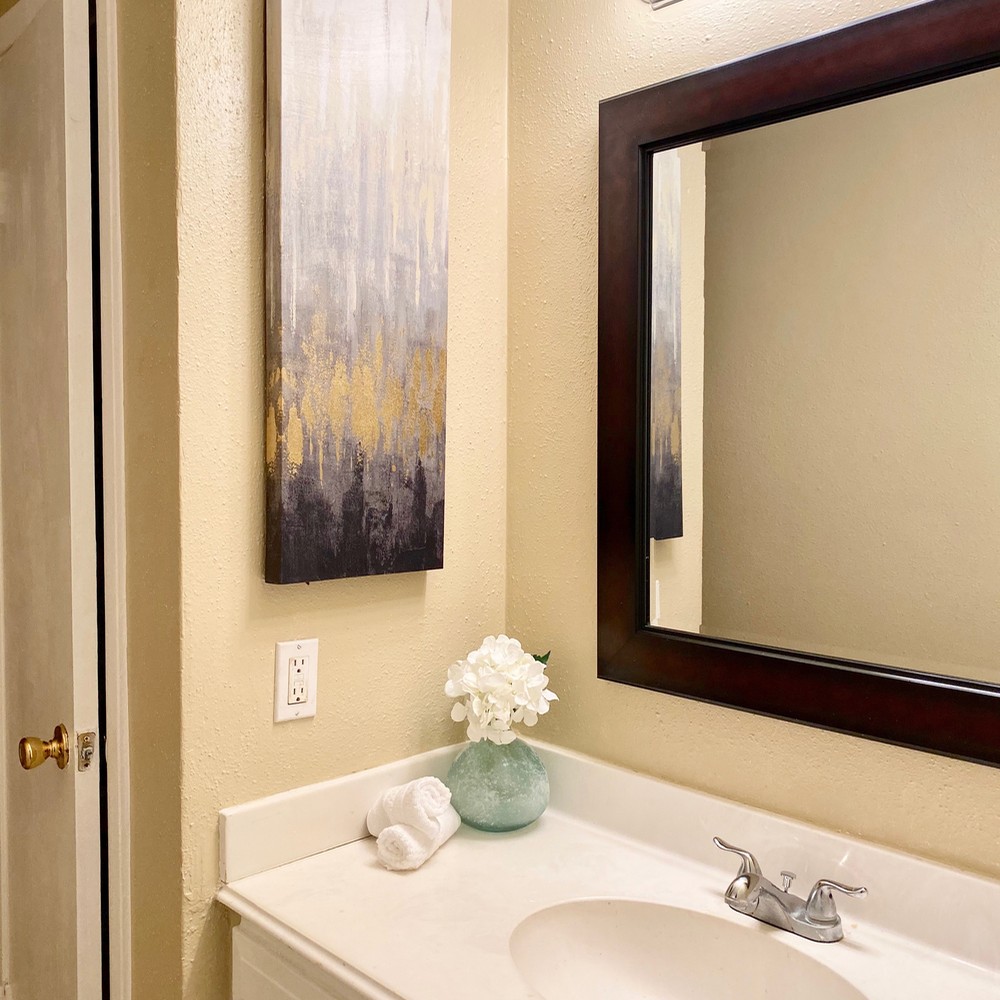 Primary bathroom with green vase with white flower. Black, gold, and white artwork.