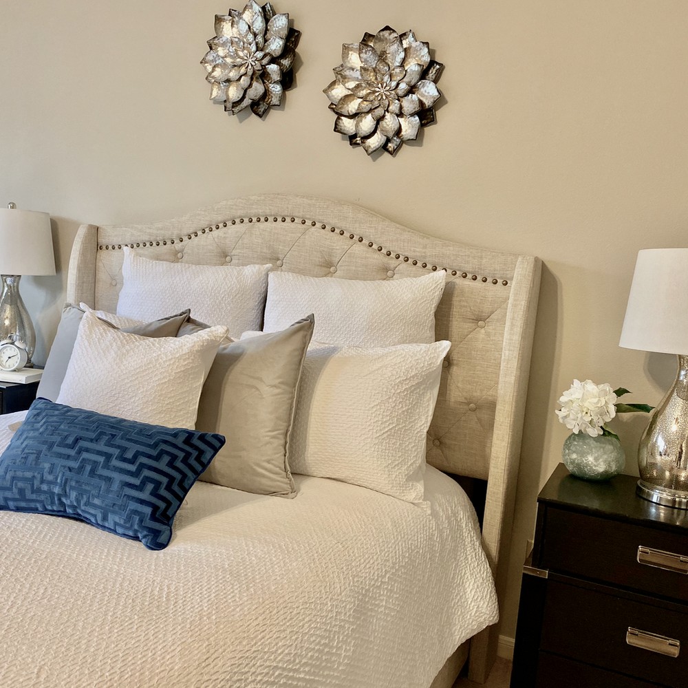 White bed with white, silver, and blue pillows. Silver flower above bed.
