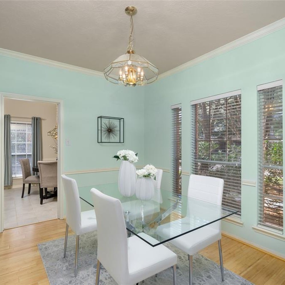 Dining room with gray rug, glass table, and four white chairs.