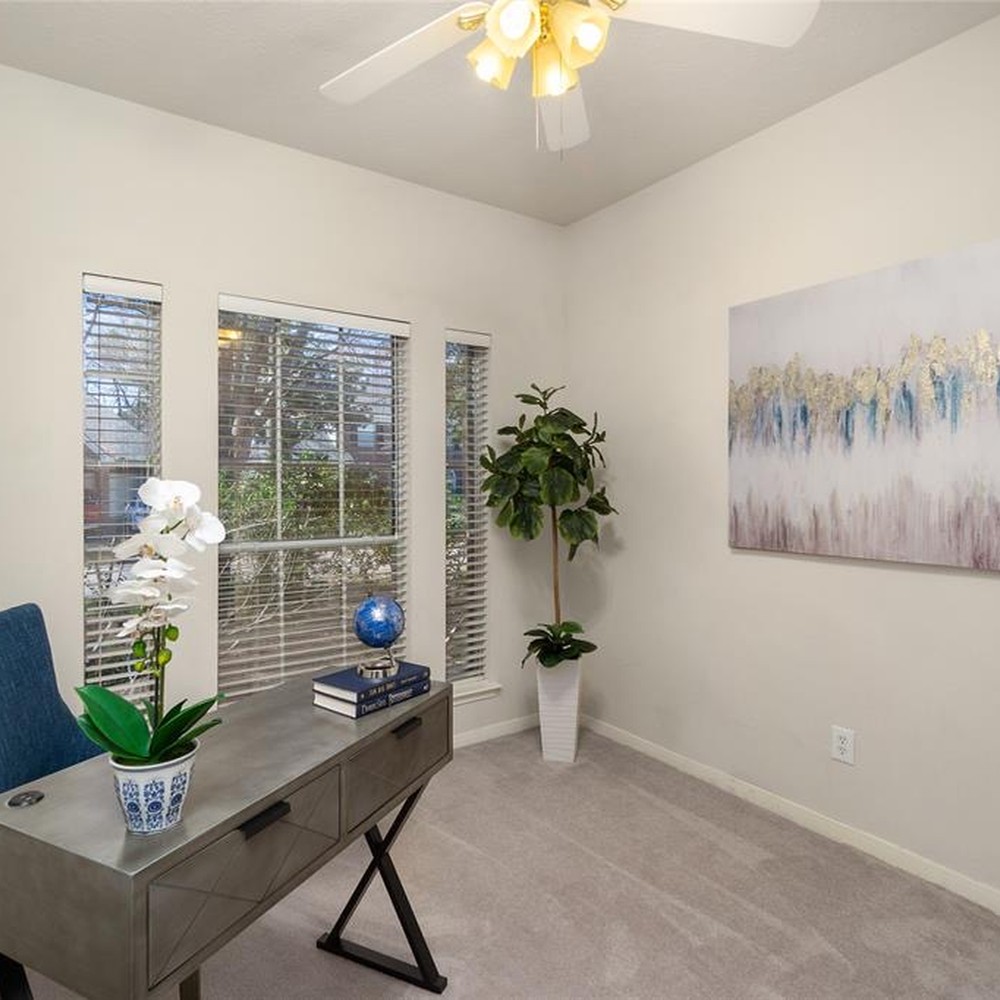 Office with gray desk, white flower, and globe. White and blue artwork. Plant in corner of room.