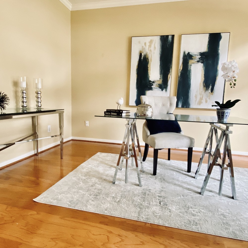 Office with glass desk and white rug. Two blue and gold artwork behind desk.