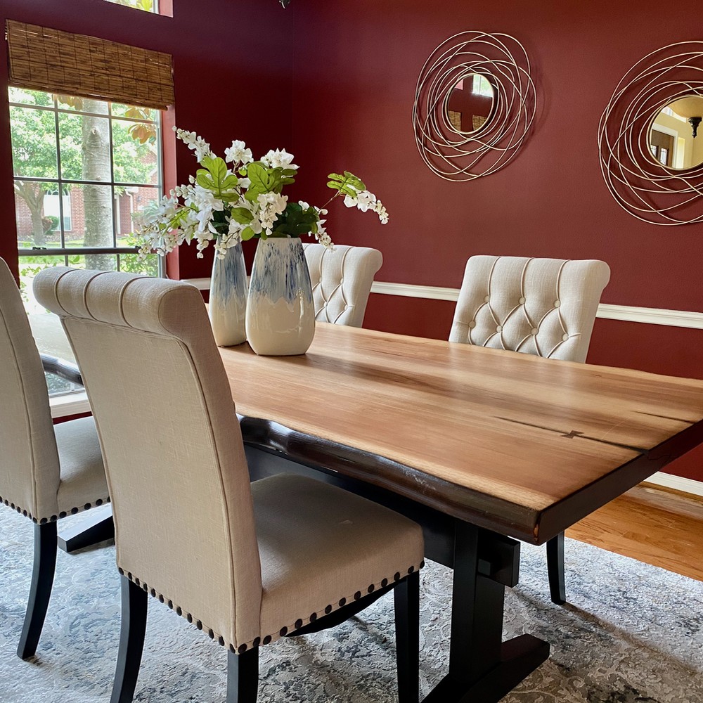 Dining room with living edge wooden table. Two blue and white vases with white flowers. Golden mirrors hung on wall.