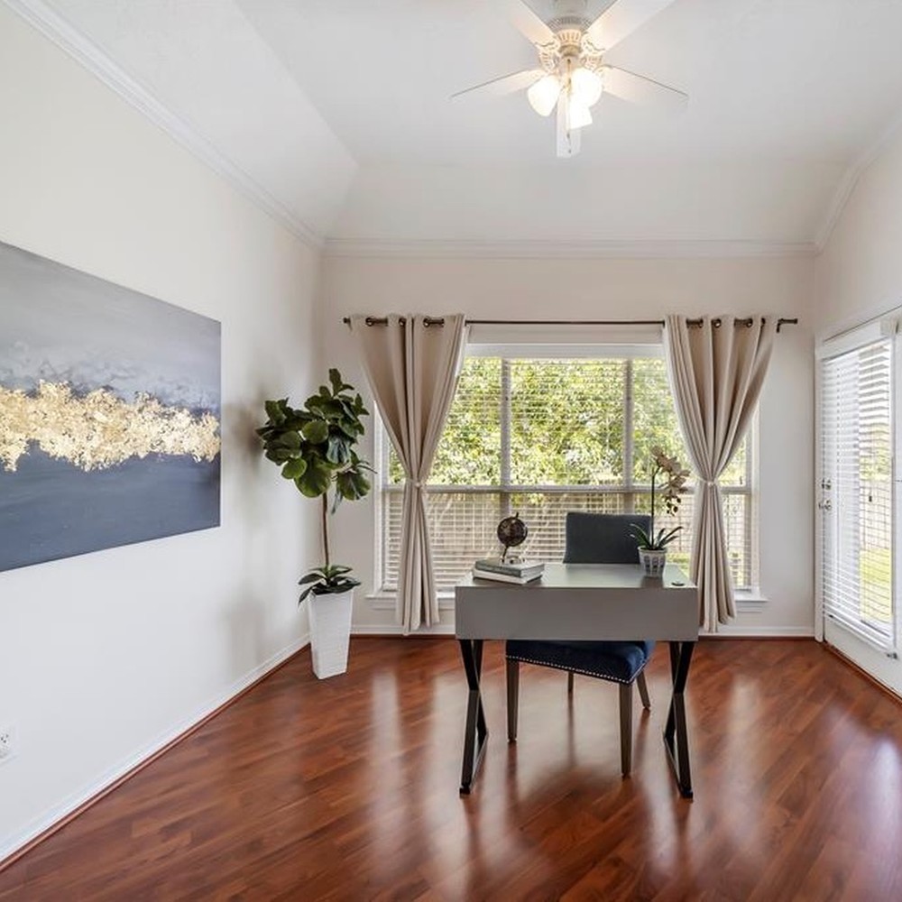 Office with light gray desk and blue chair. Gray and gold artwork beside desk. Plant in corner of room.