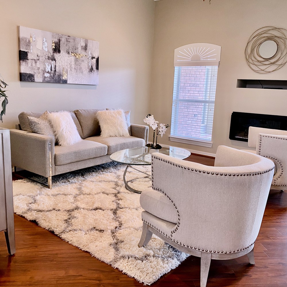 Living room with artwork above sofa. Two white chairs, white rug.