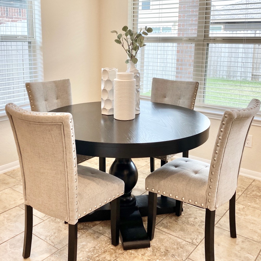 Black round breakfast table with four light gray chairs. Three white vases displayed on the table.