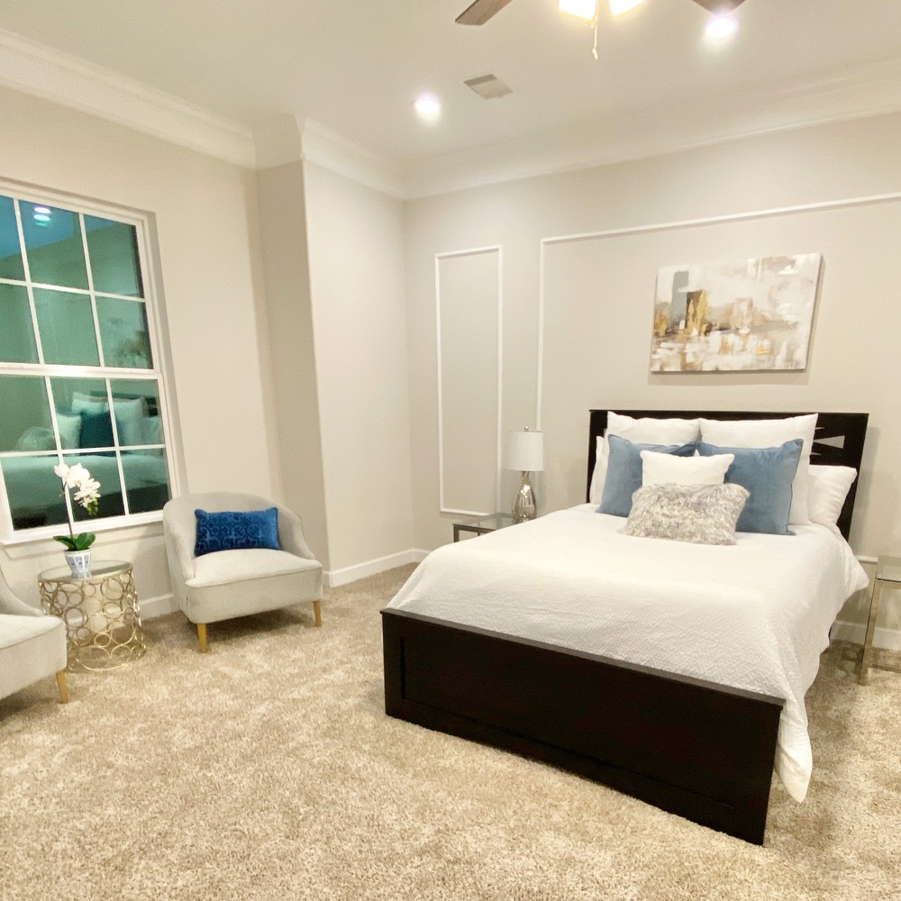 Primary bedroom with black bed frame and white comforter. Two chairs with blue pillows.