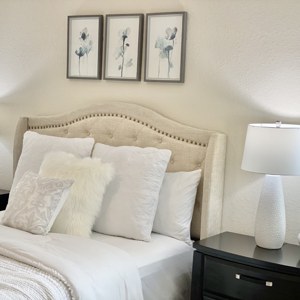 Primary bedroom with white bed. Three blue flower artwork displayed above the bed.