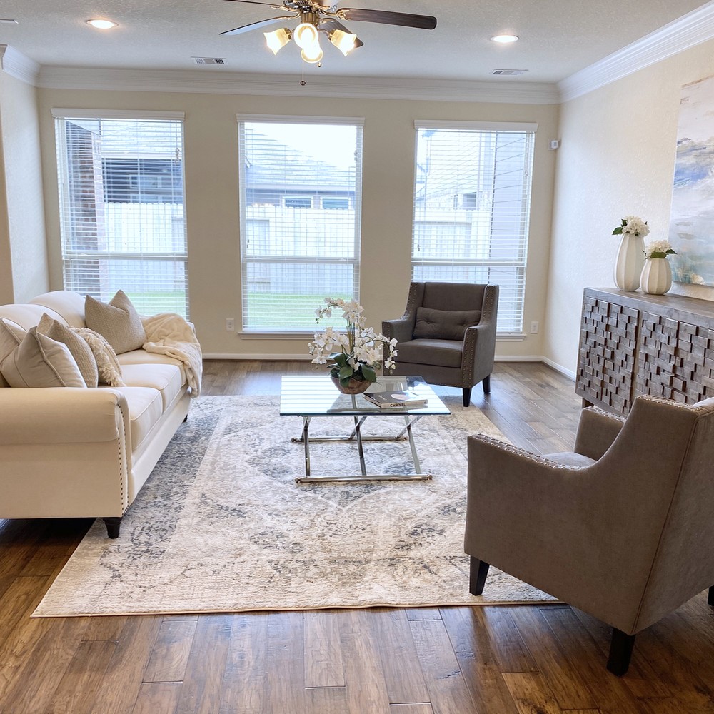 White and gray rug, and two large dark gray chairs. White sofa, glass coffee table, and wooden cabinet.