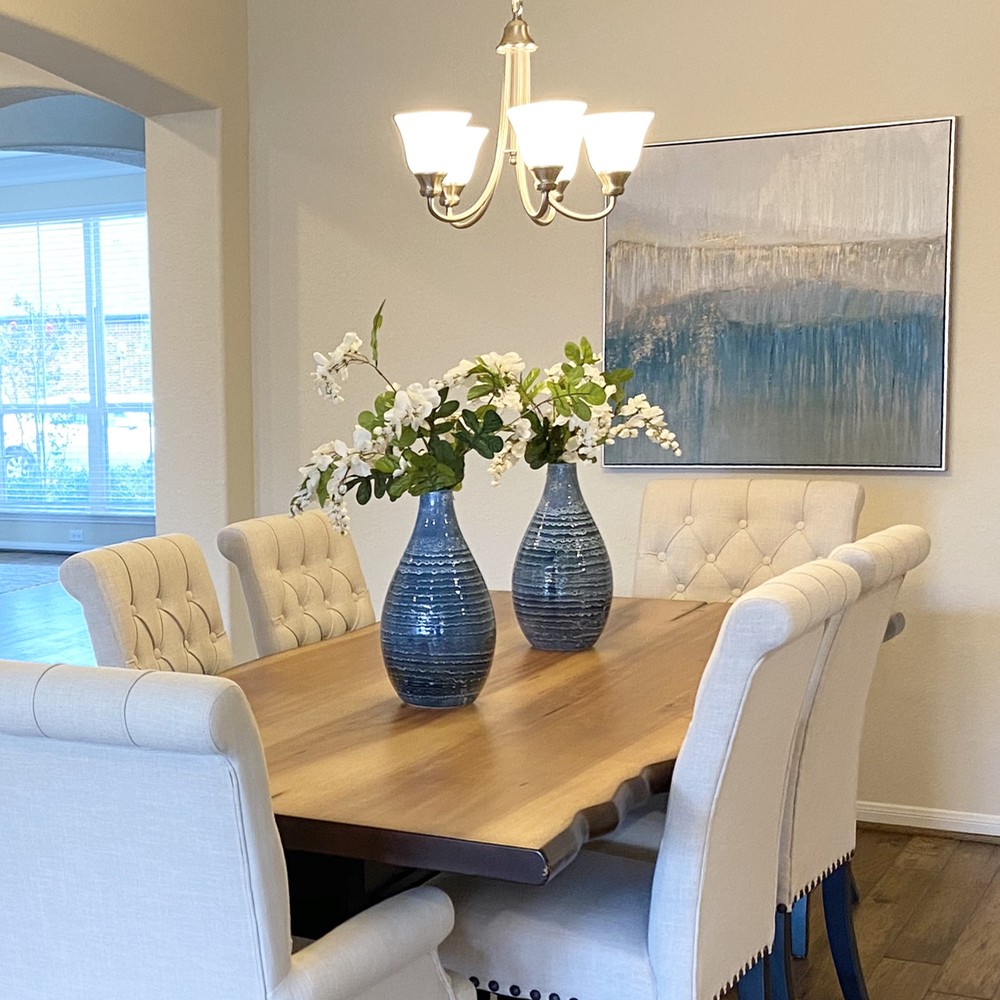 Living edge wooden table with two blue vases with white flowers. Blue artwork displayed in this dining room.