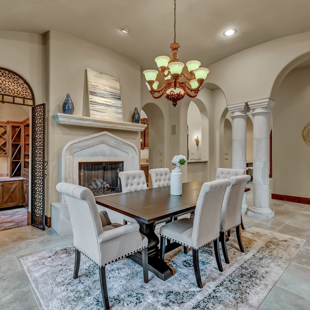Dining room with dark wooden table, six white chairs, and white vase with white flowers. Fireplace with blue vases and artwork.