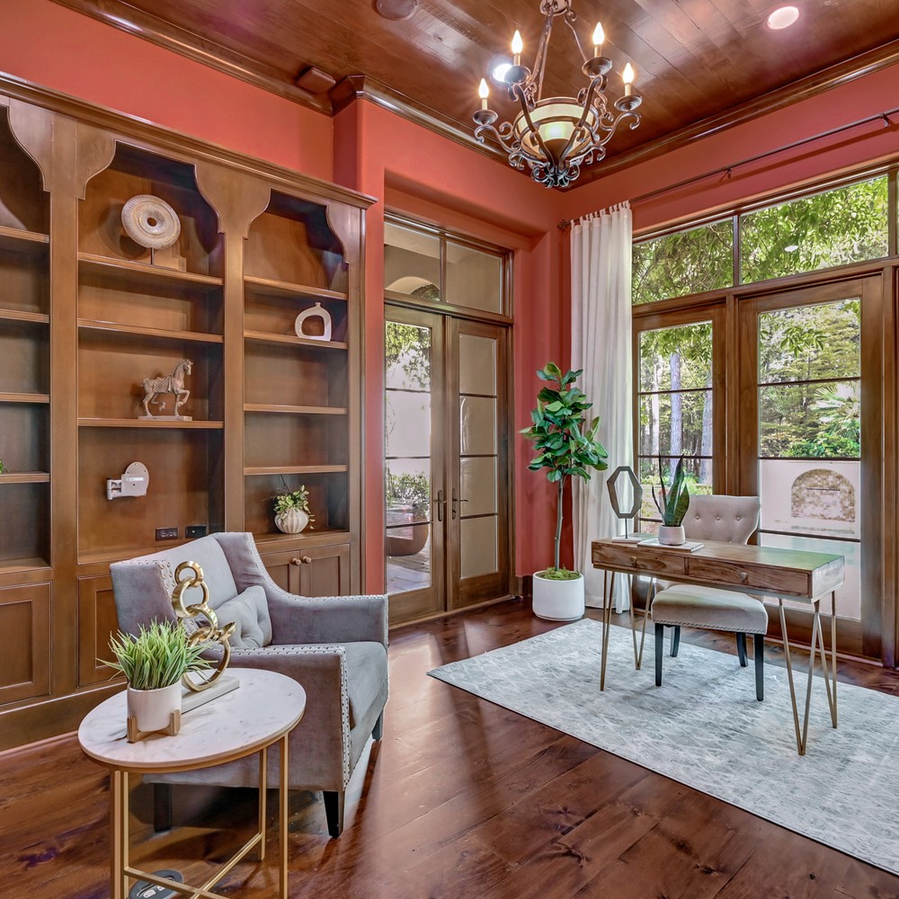 Office with built in cabinets. Accessores placed in the cabinets. Wooden desk in front of windows, and chair and side table in front of desk.