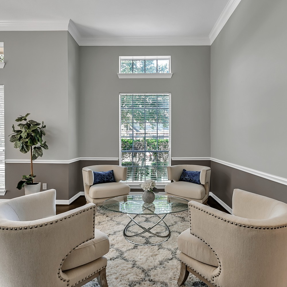 Sitting room with four large white chairs, highlighted by blue pillows. White and gray rug, and glass coffee table.