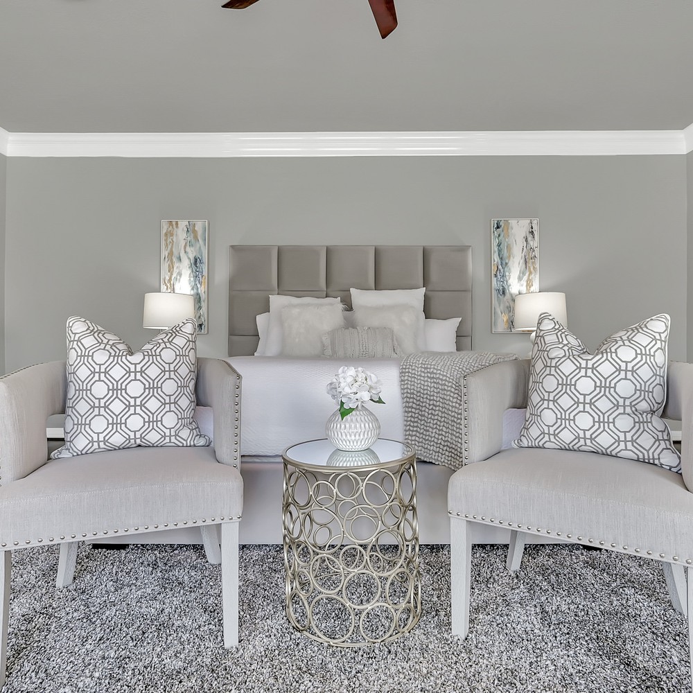 Primary bedroom with gray textered bed frame, and white comforter. Two chairs with white patterned pillows.