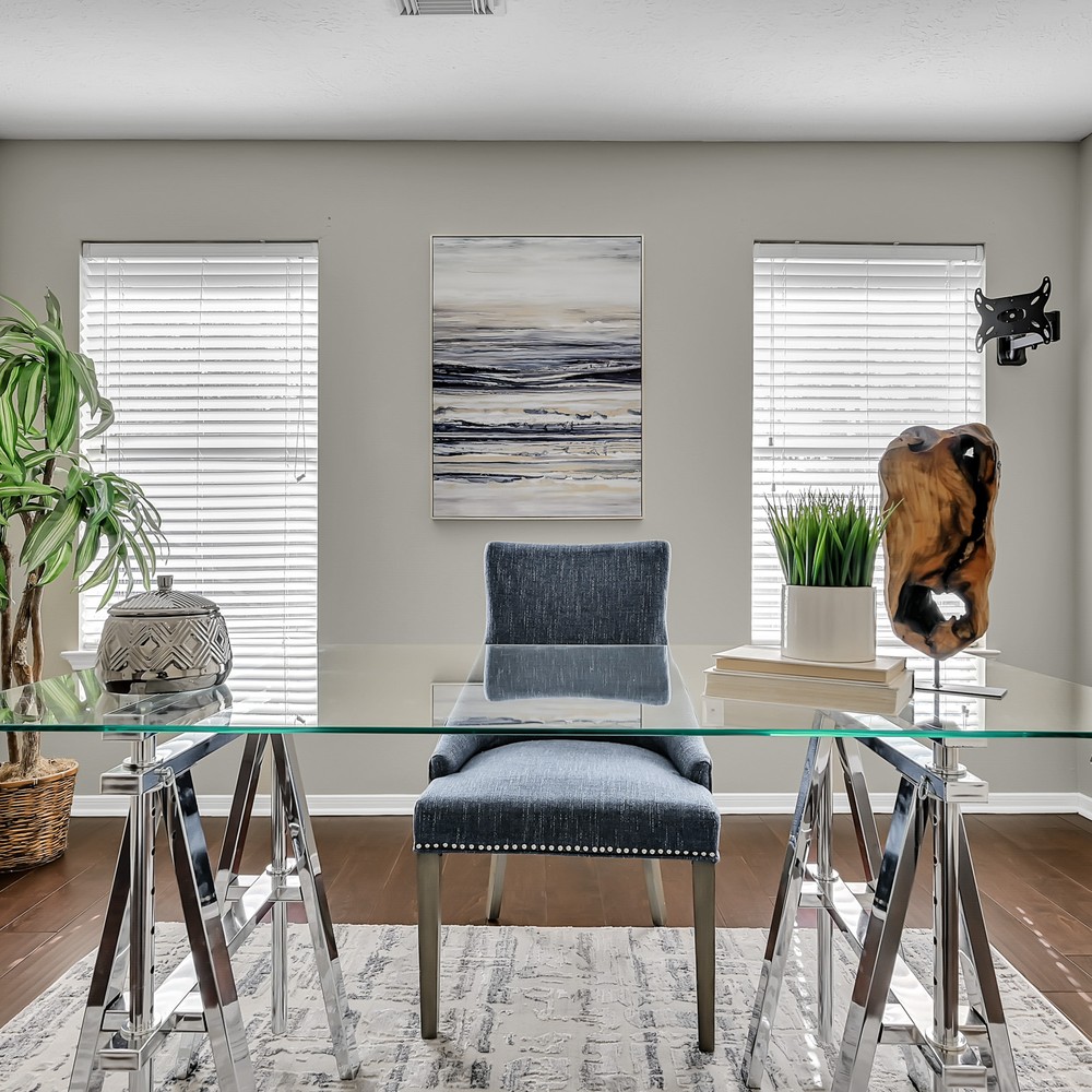 Office with glass desk and silver frame. Blue chairs with blue art.