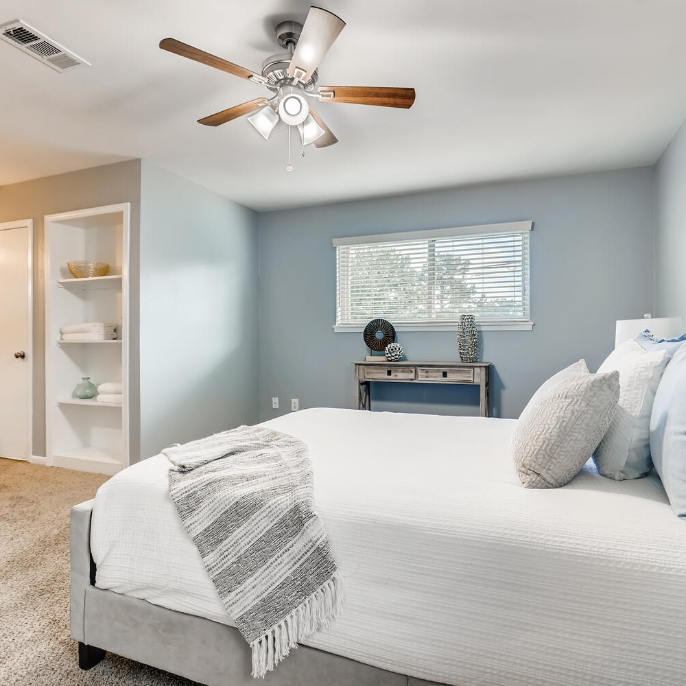 Primary bedroom with gray bed frame, white comforter, gray and white throw, and pillows. Console table with accessories.