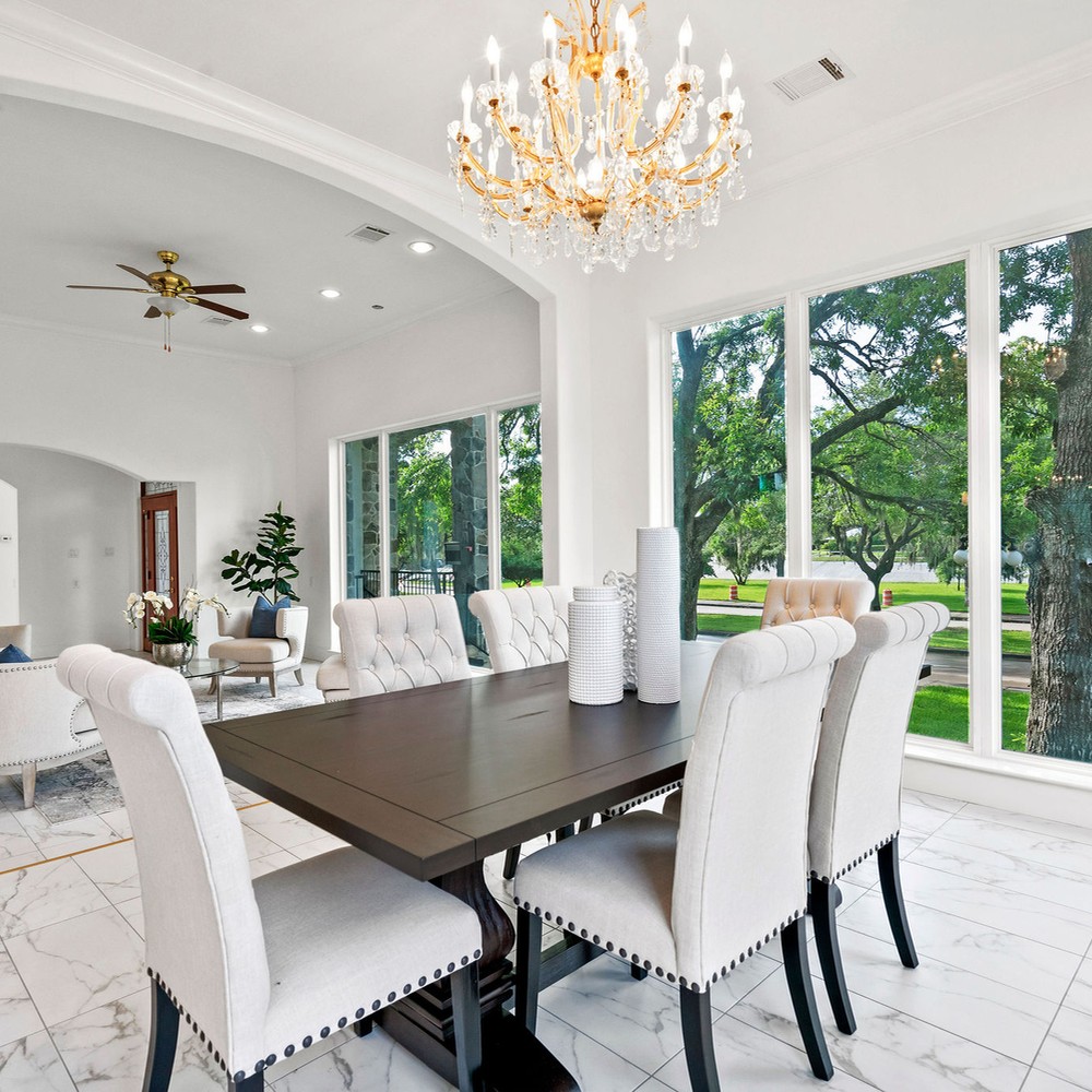 Dining room with wooden table and white chairs, surrounded by windows.