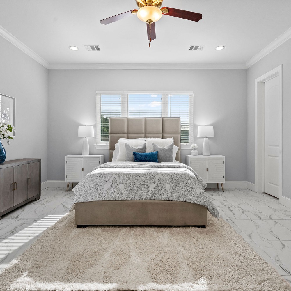 Primary bedroom with white rug, bed with white comforter, and blue pillows.