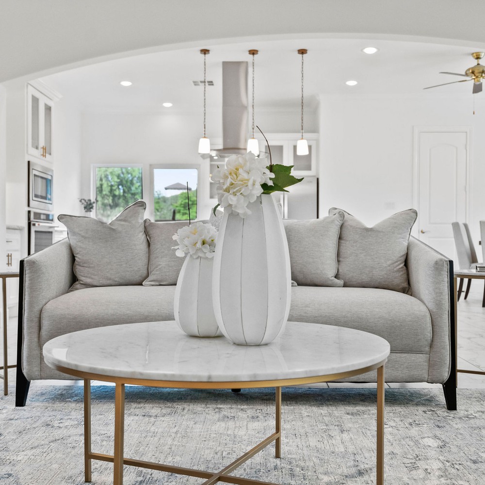 Living room with light gray sofa and white marble coffee table. White vases on the coffee table with flowes.