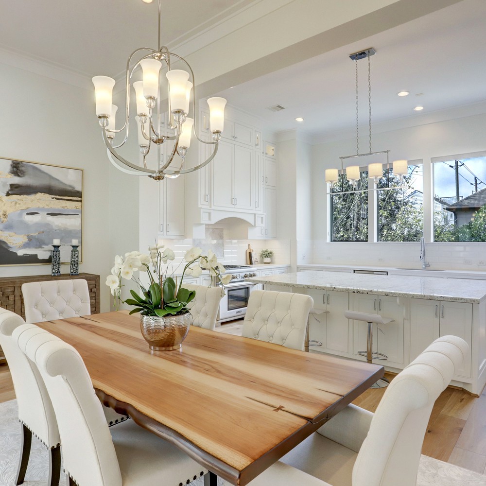 Close up image of wood table and six white chairs. Flower arangement on top of table. Console and art in background.