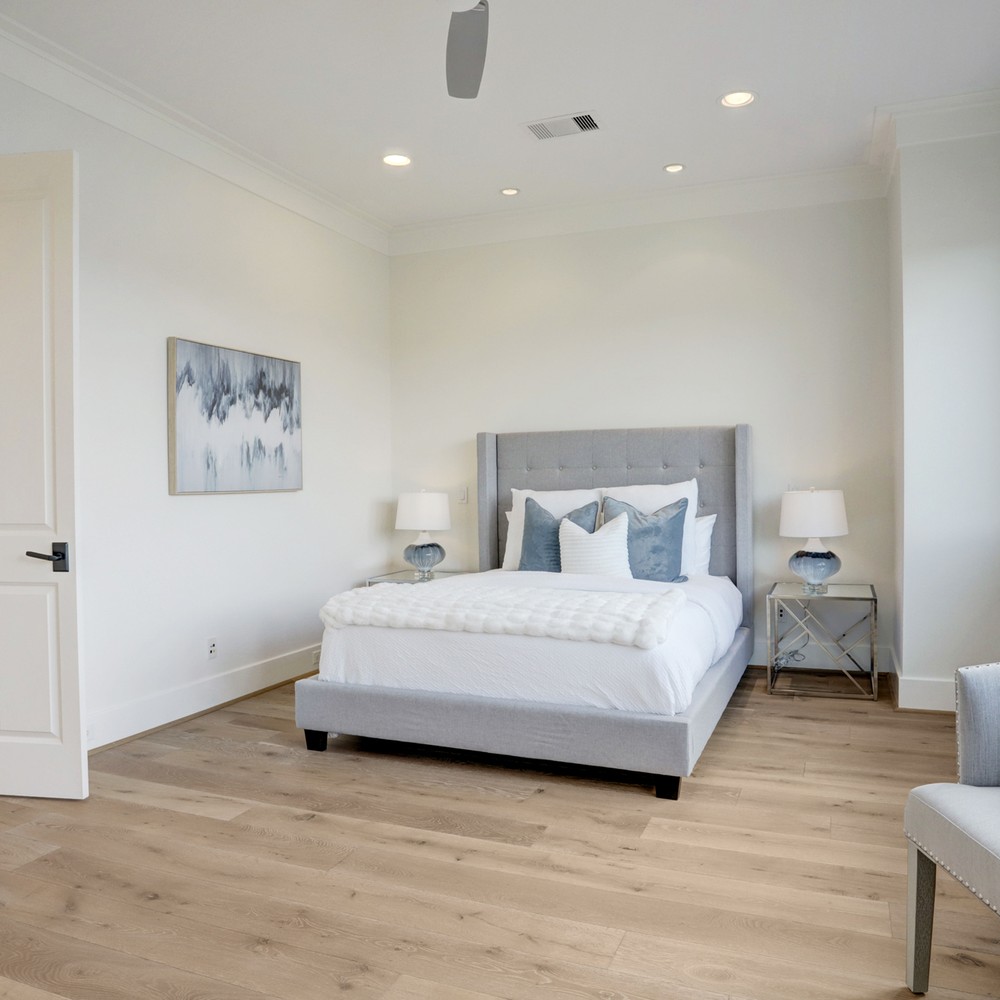 Primary bedroom with grey bed, white comforter, and blue pillows. Blue art on wall.