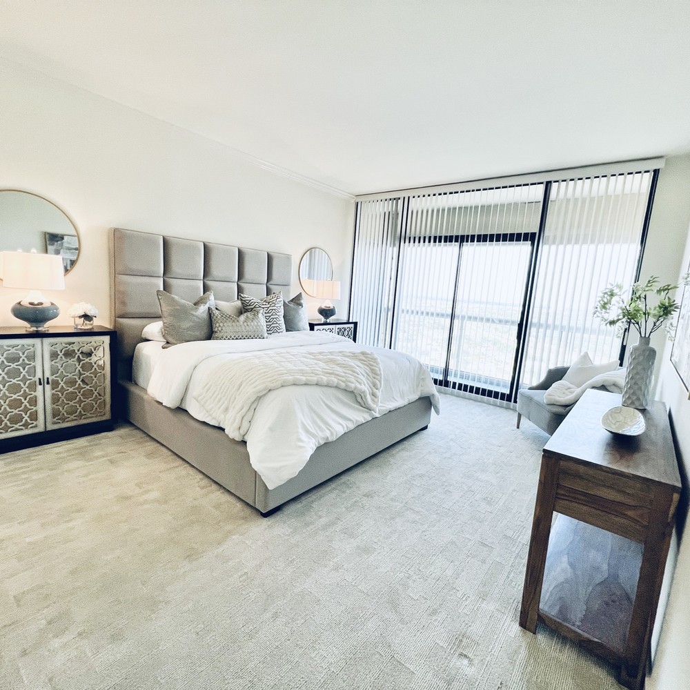 Primary bedroom with gray bed, white comforter, two black and gold nightstands, and wood console.