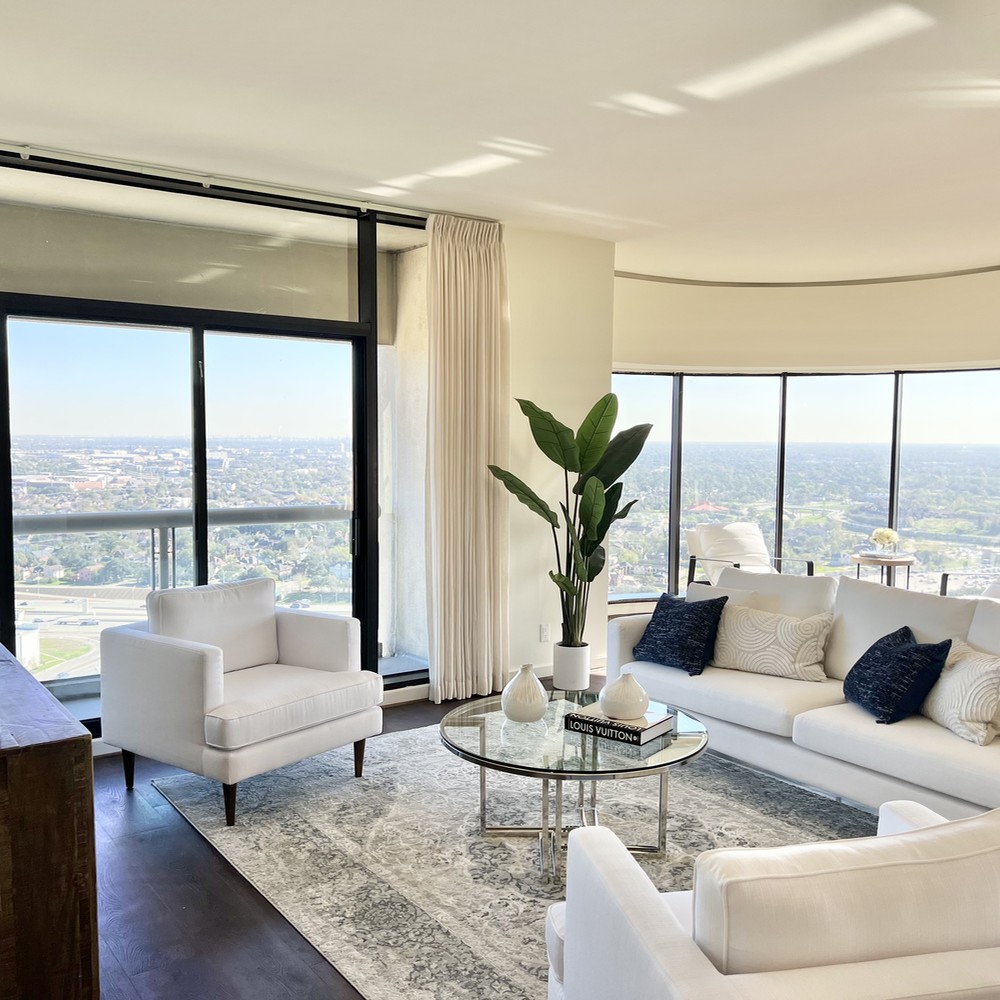 Living room with two white chairs, glass coffee table, white sofa and plant.