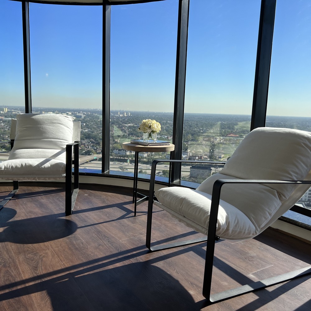 Two white chairs with black metal frames. Side table with flower. View of the sky line.