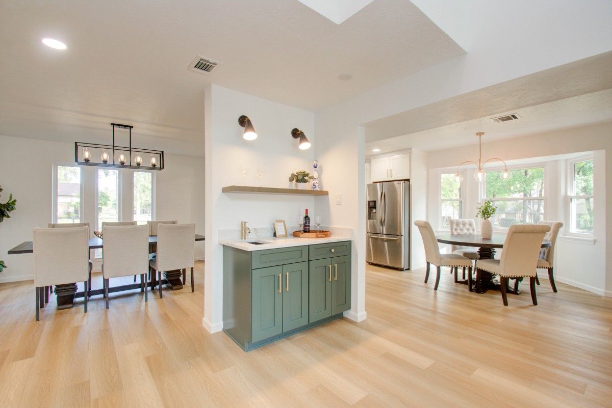 This space features a bar area. The cabinets are painted a beautiful sage green. Wine with glasses and additional accessories are showcased.